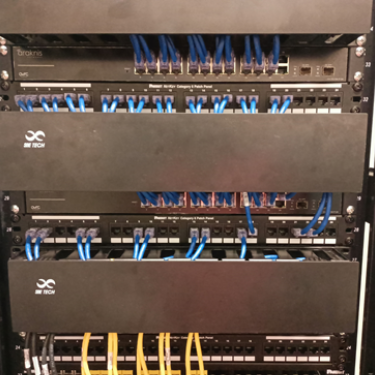 Vista frontal de un rack de telecomunicaciones que organiza switches Araknis y paneles de parcheo (patch panels) Panduit con cableado estructurado azul.